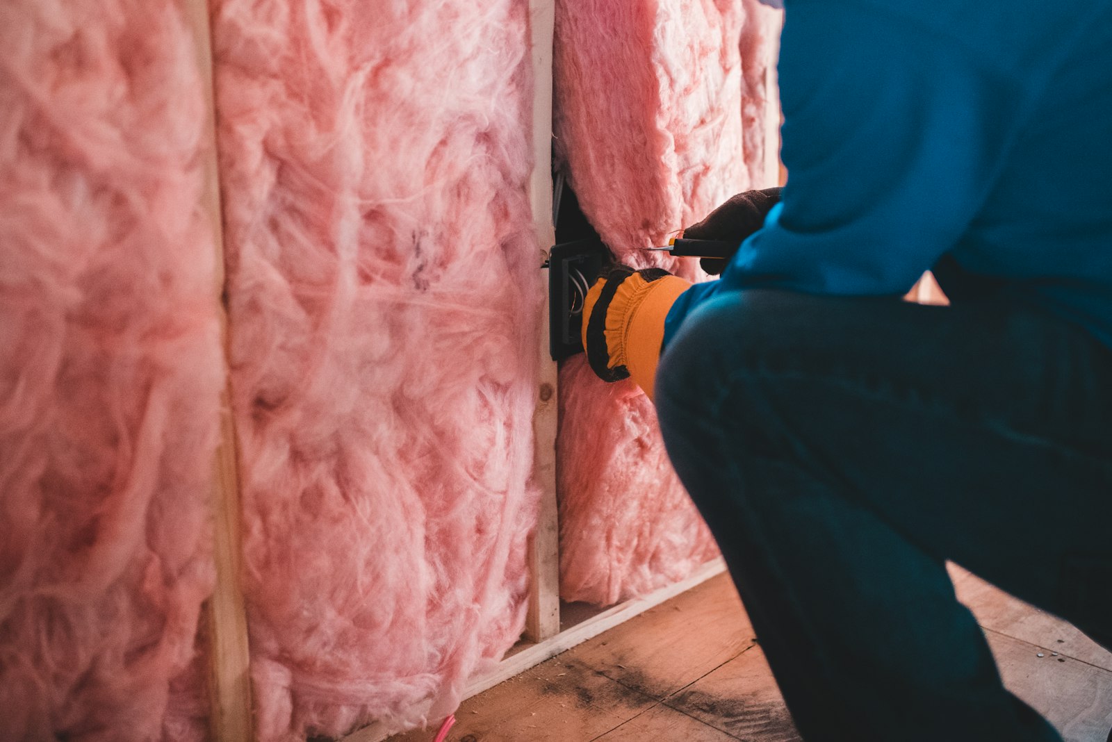 Artisan posant un isolant en laine de verre rose dans une ossature de mur
