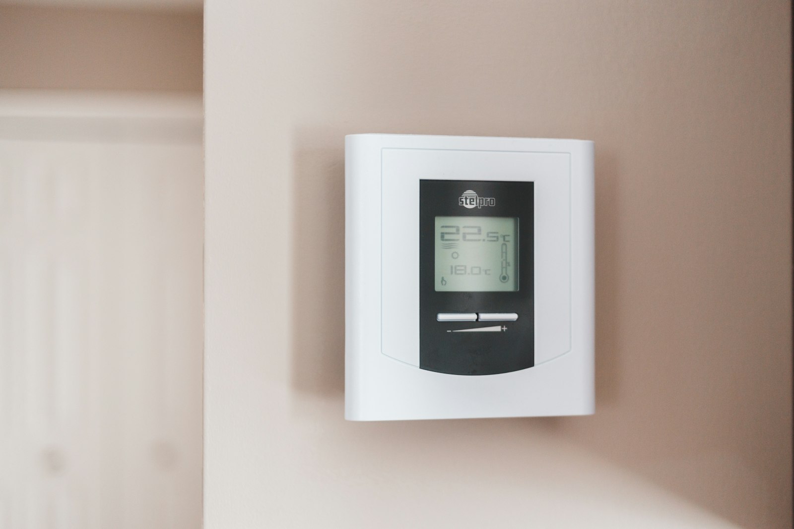 Thermostat mural blanc et gris affichant 19,5°C, illustrant le réglage de la température par pièce