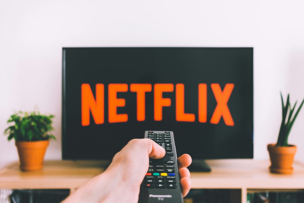 Main tenant une télécommande pointée vers un écran de télévision pour choisir un service de streaming